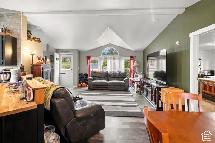 Vaulted ceiling with exposed beams, wood-finish flooring, half-wall with butcher block countertop, arched window, and a paneled entry door
