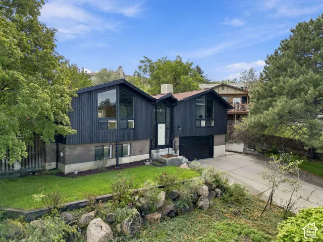 Split-level residence featuring dark vertical siding, a two-car garage, and a concrete driveway