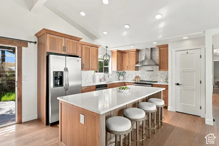 Kitchen featuring wood-finish cabinetry, stainless steel appliances, a center island with seating, a tile backsplash, and recessed lighting