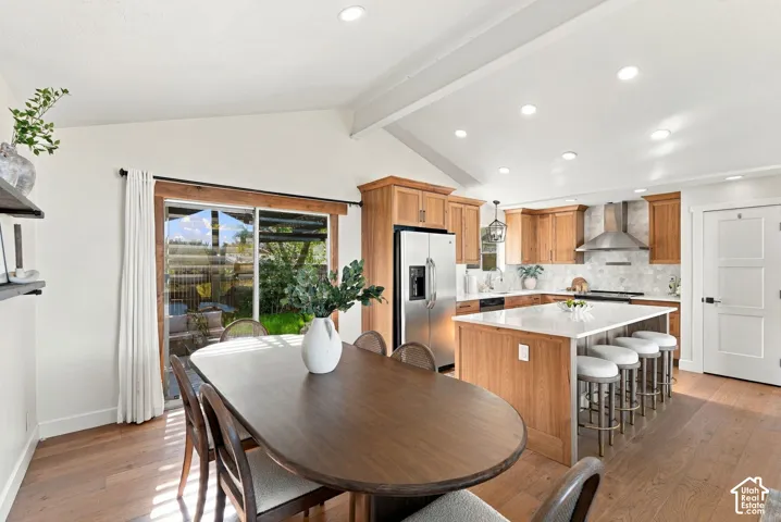 Vaulted ceilings with exposed beams, stainless steel appliances, a center island with seating, wood-finish flooring, and a sliding glass door