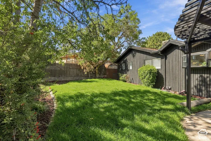 Expansive backyard featuring a manicured lawn, established perimeter landscaping, and a slatted pergola structure