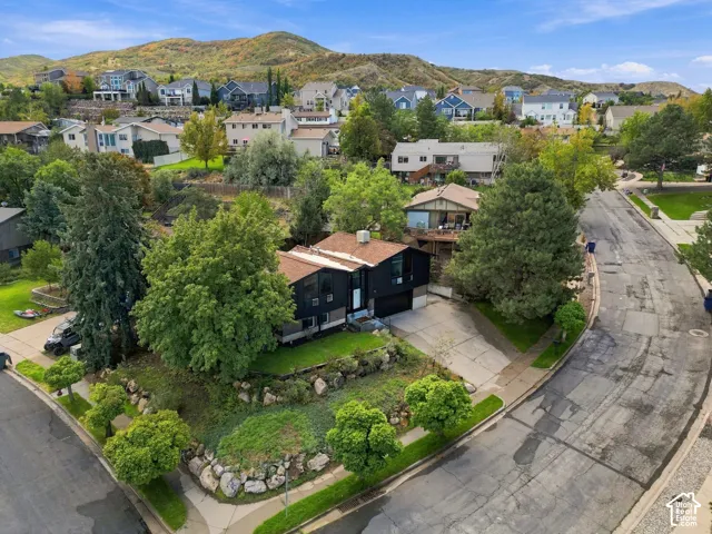 Two-story dark-clad exterior with a brown roof, concrete driveway, and established front yard landscaping featuring mature trees and natural stone accents