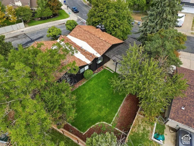 Asphalt shingle roof, black exterior siding, mature trees, manicured lawn, and a covered patio area