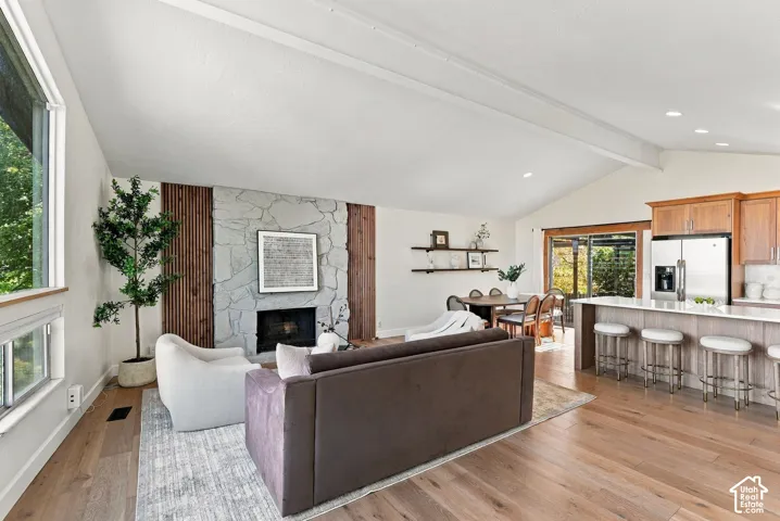 Vaulted ceilings with exposed beams, stone-faced fireplace, wood-finish flooring, and a kitchen island with seating