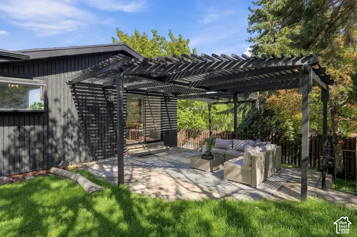 Expansive patio featuring a large pergola, concrete pavers, and a sliding glass door entry to the residence