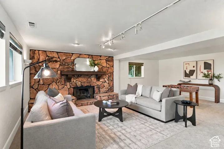 Stone-surround fireplace with a wood mantle, track lighting, recessed lighting, windows with blinds, and light-toned carpeting