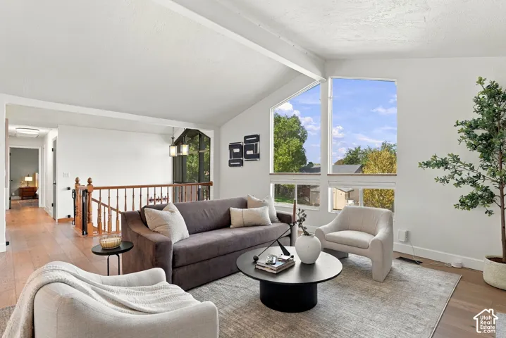 Vaulted ceilings with exposed beams, wood-finish flooring, two-story windows, and a wood railing with balusters