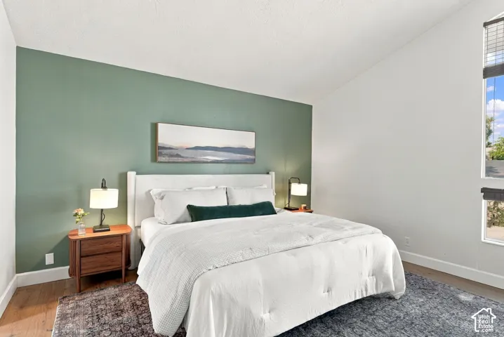 Vaulted ceiling, accent wall, wood-finish flooring, tall window, and wood nightstand with drawers