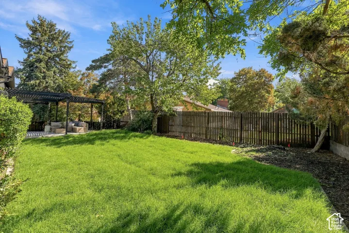 Expansive lawn area with a dark wood pergola, stone patio, and mature trees