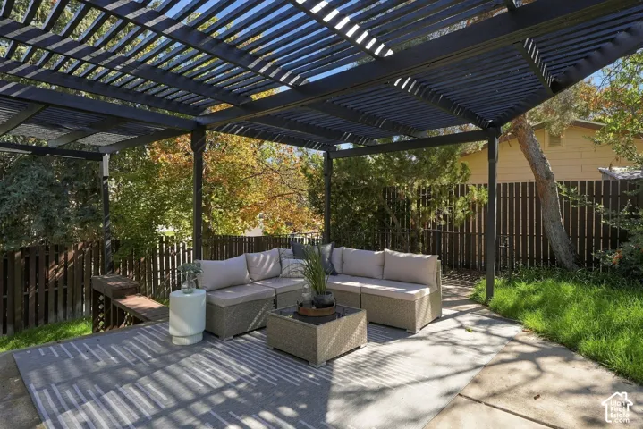 Expansive concrete patio featuring a dark-toned pergola, a wood fence, and a grass area