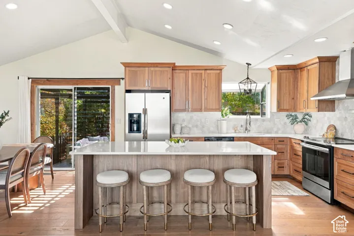 Vaulted ceiling with exposed beam, wood-finish flooring, kitchen island with countertop, stainless steel appliances, and sliding glass door