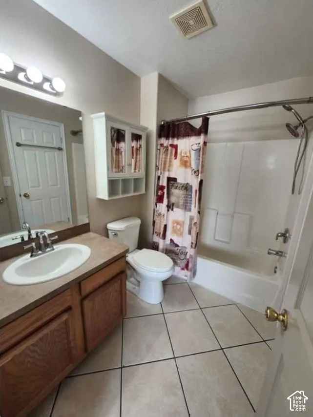 Bathroom featuring a white toilet, built-in vanity with integrated sink, wood-finish cabinetry, and tiled flooring