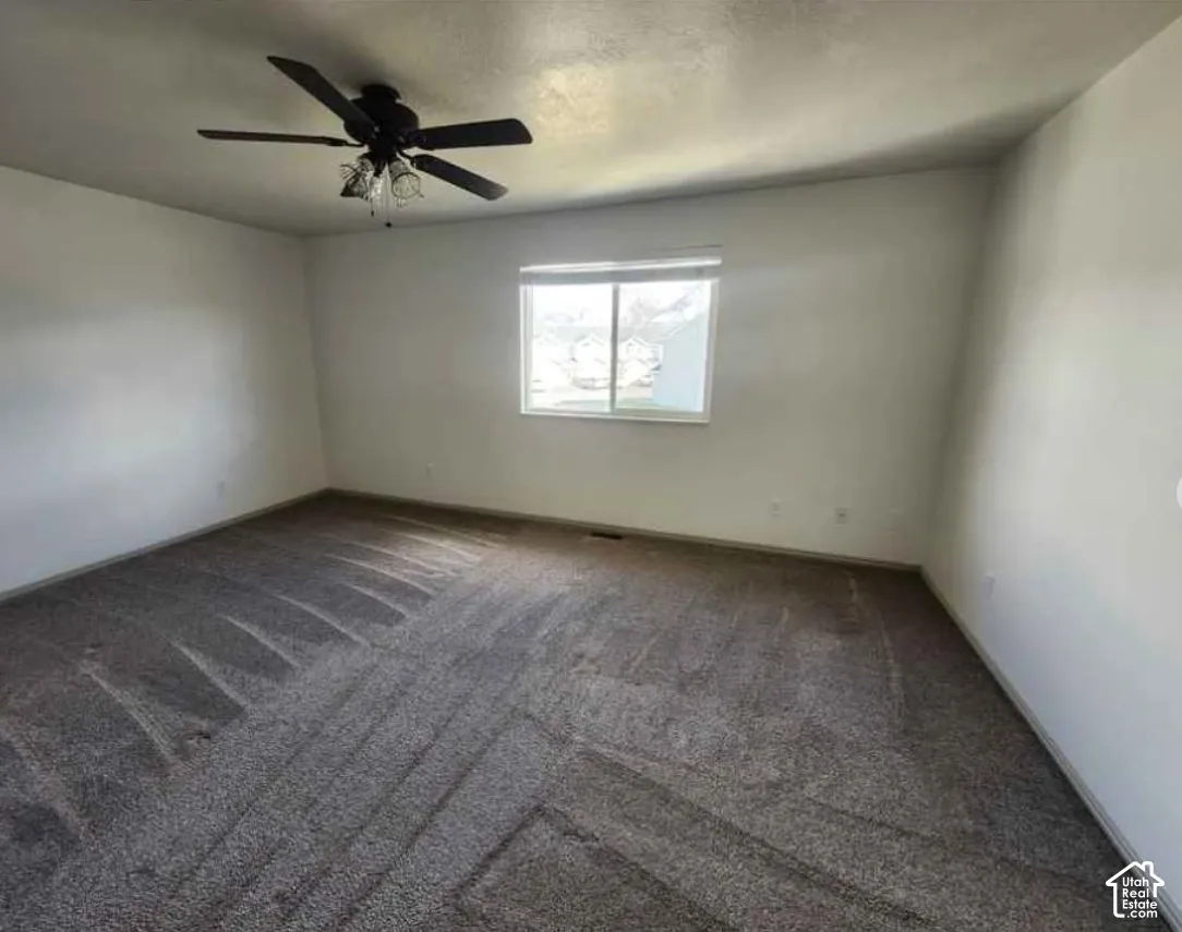 Spacious room featuring neutral carpeting, white wall finishes, a window, and a ceiling fan with integrated lighting