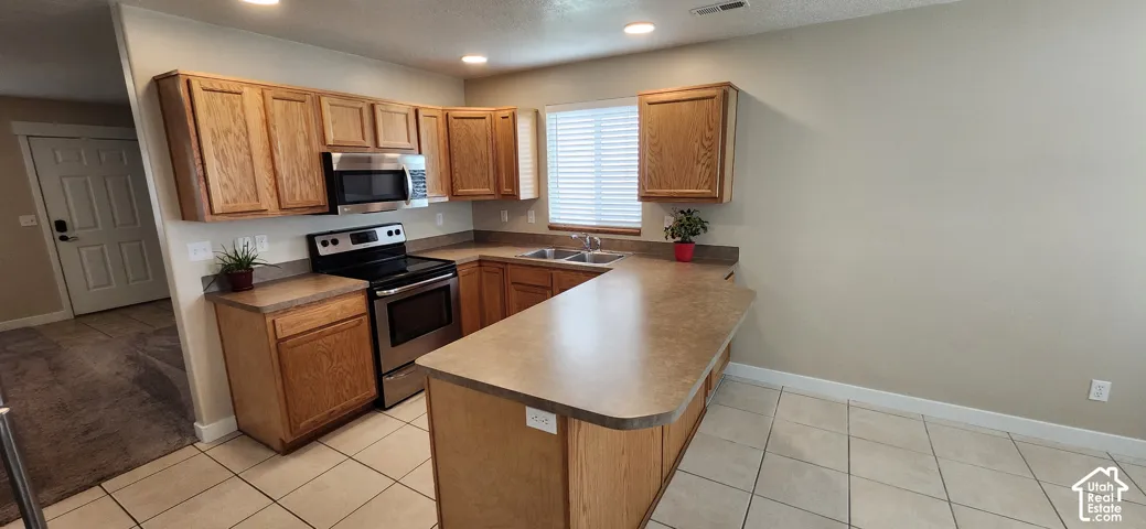 U-shaped kitchen featuring wood cabinetry, stainless steel appliances, a double basin sink, and tile flooring