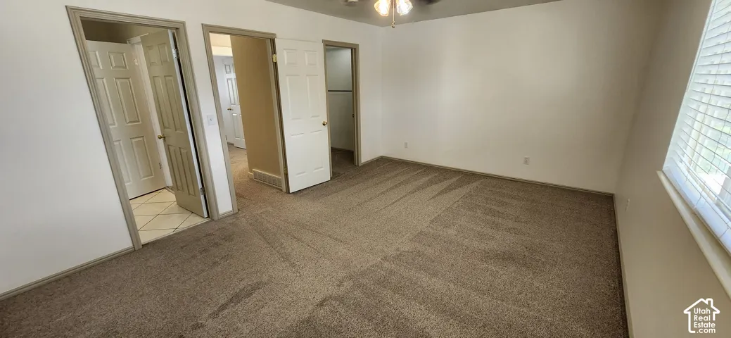 Spacious room with neutral-toned carpet, white walls, multiple doorways, and a window with blinds