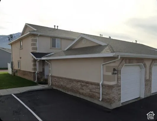 Stucco exterior with brick veneer detailing, attached garage, gabled roofline, and paved parking area