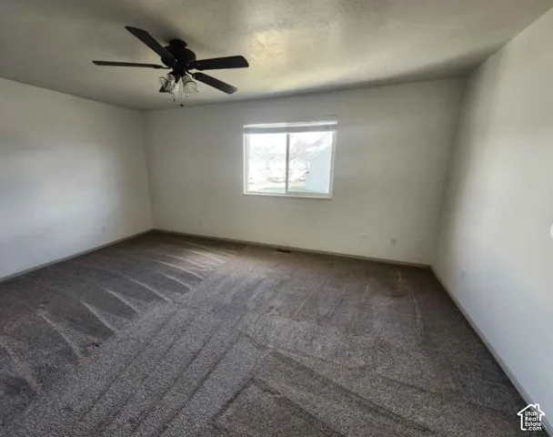 Spacious room featuring neutral carpeting, white wall finishes, a window, and a ceiling fan with integrated lighting