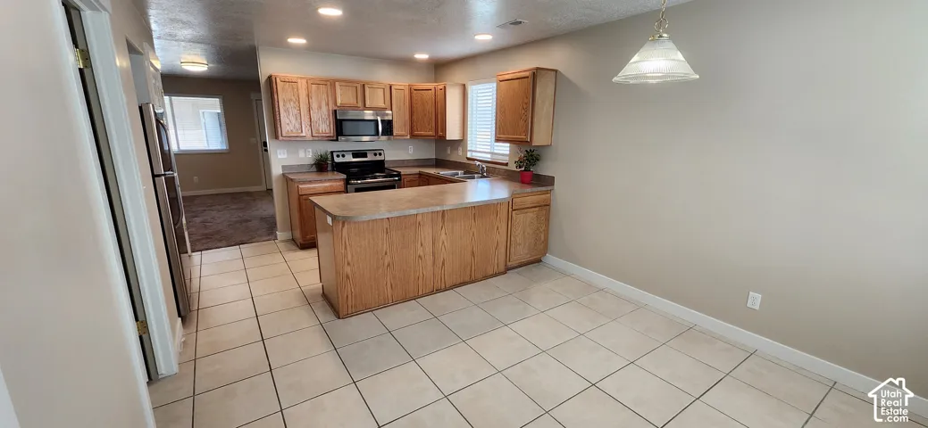 Kitchen featuring wood cabinetry, stainless steel appliances, a center island with countertop seating, and tile flooring