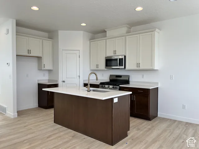 Central kitchen island with a built-in sink, stainless steel appliances, two-tone cabinetry, light-toned countertops, and wood-finish flooring