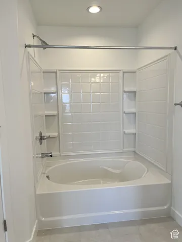 Bathtub with an integrated shower, tiled surround, built-in shelving, and recessed lighting