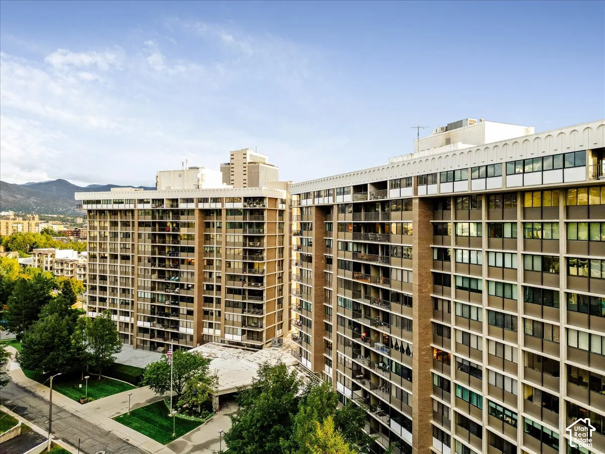 High-rise building with multiple private balconies, a ground-level entrance with a covered drop-off area, and surrounding green spaces