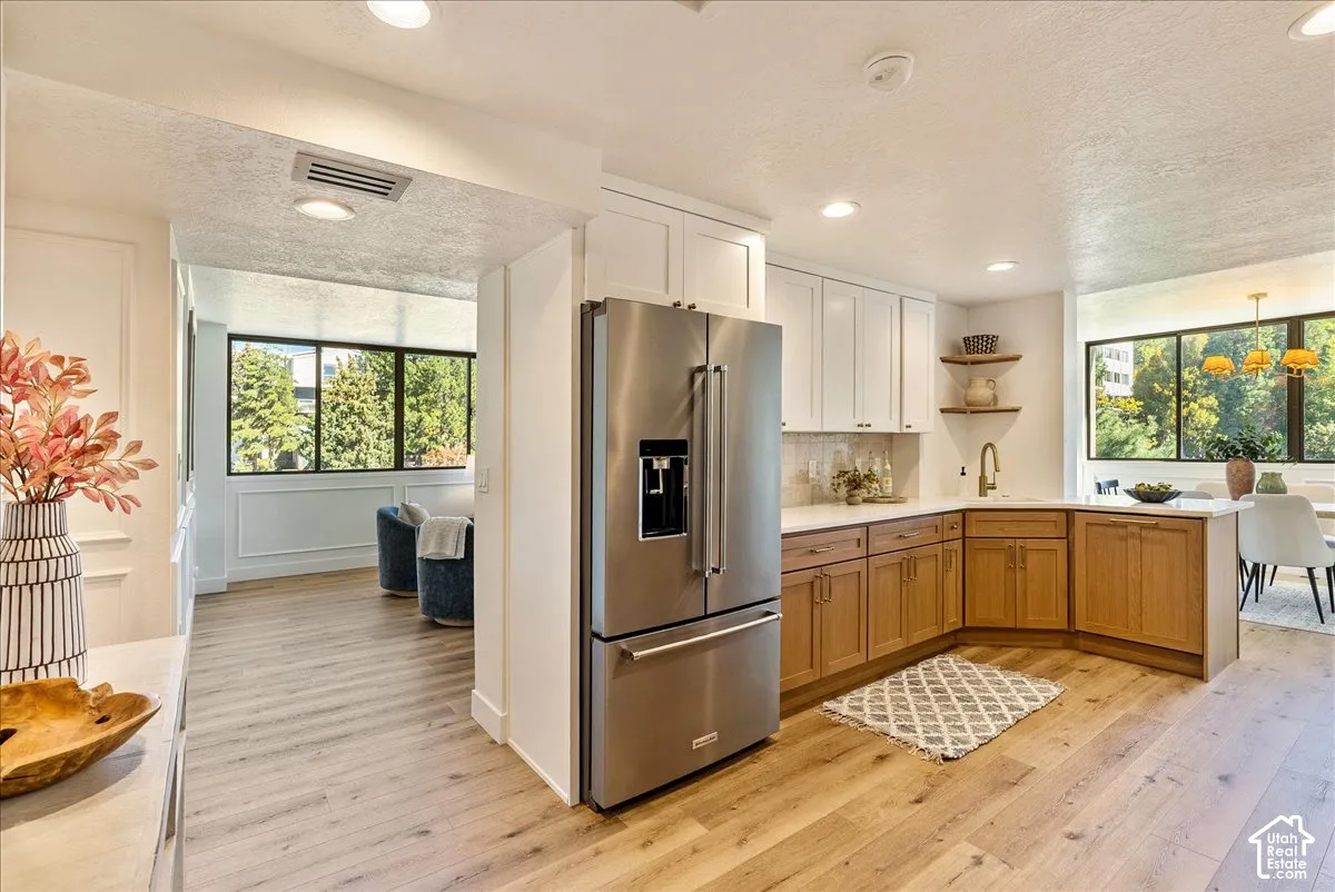 Kitchen featuring stainless steel refrigerator, white upper cabinetry, wood-finish lower cabinetry, and wood-finish flooring