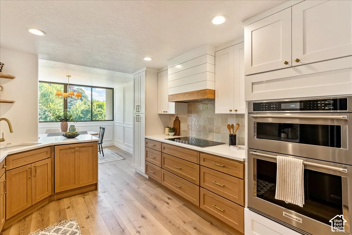 Modern kitchen featuring wood-finish flooring, white perimeter cabinetry, wood-tone island cabinetry, stainless steel built-in double ovens, and a tile backsplash