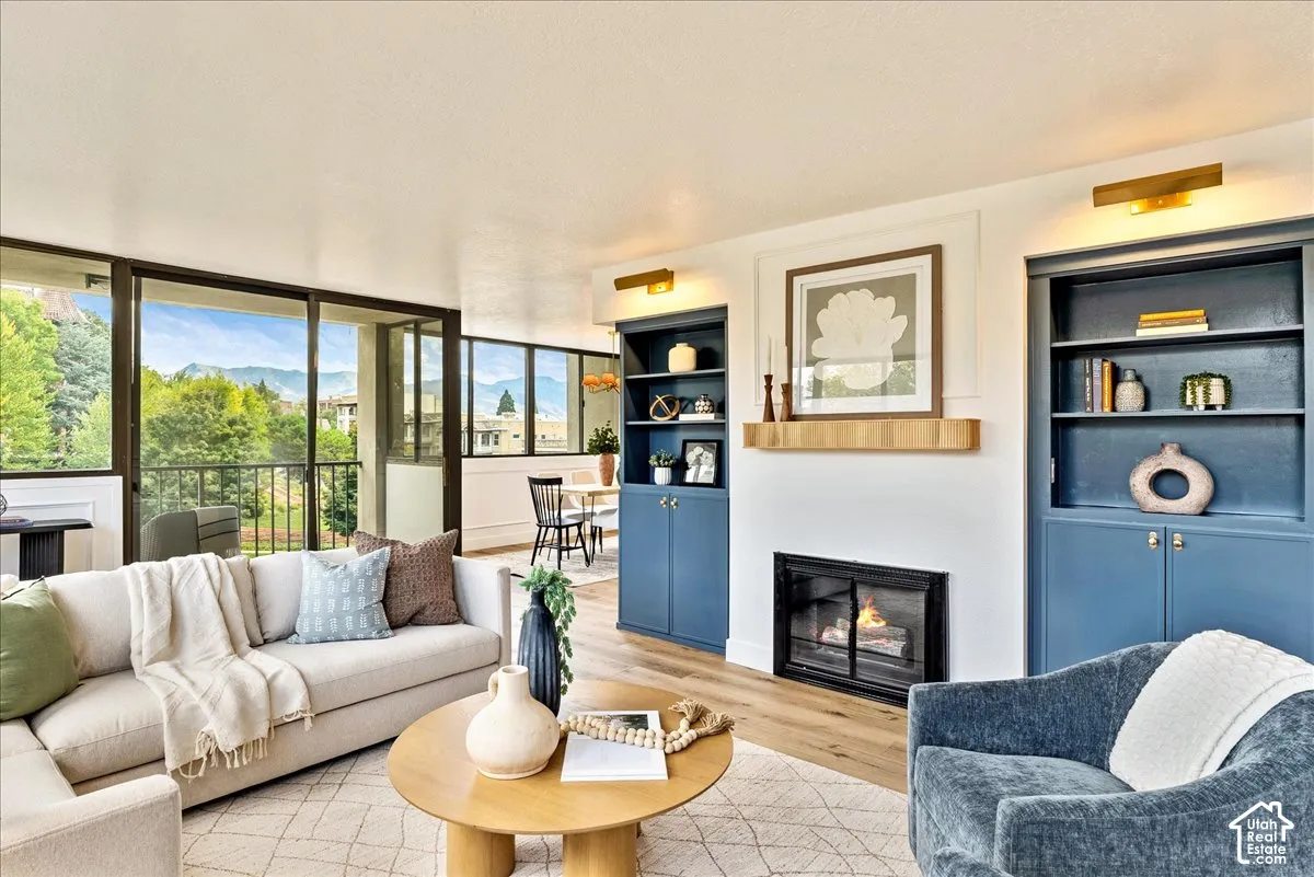 Living area featuring wood-finish flooring, a fireplace with a wood mantle, and built-in shelving with lower cabinetry