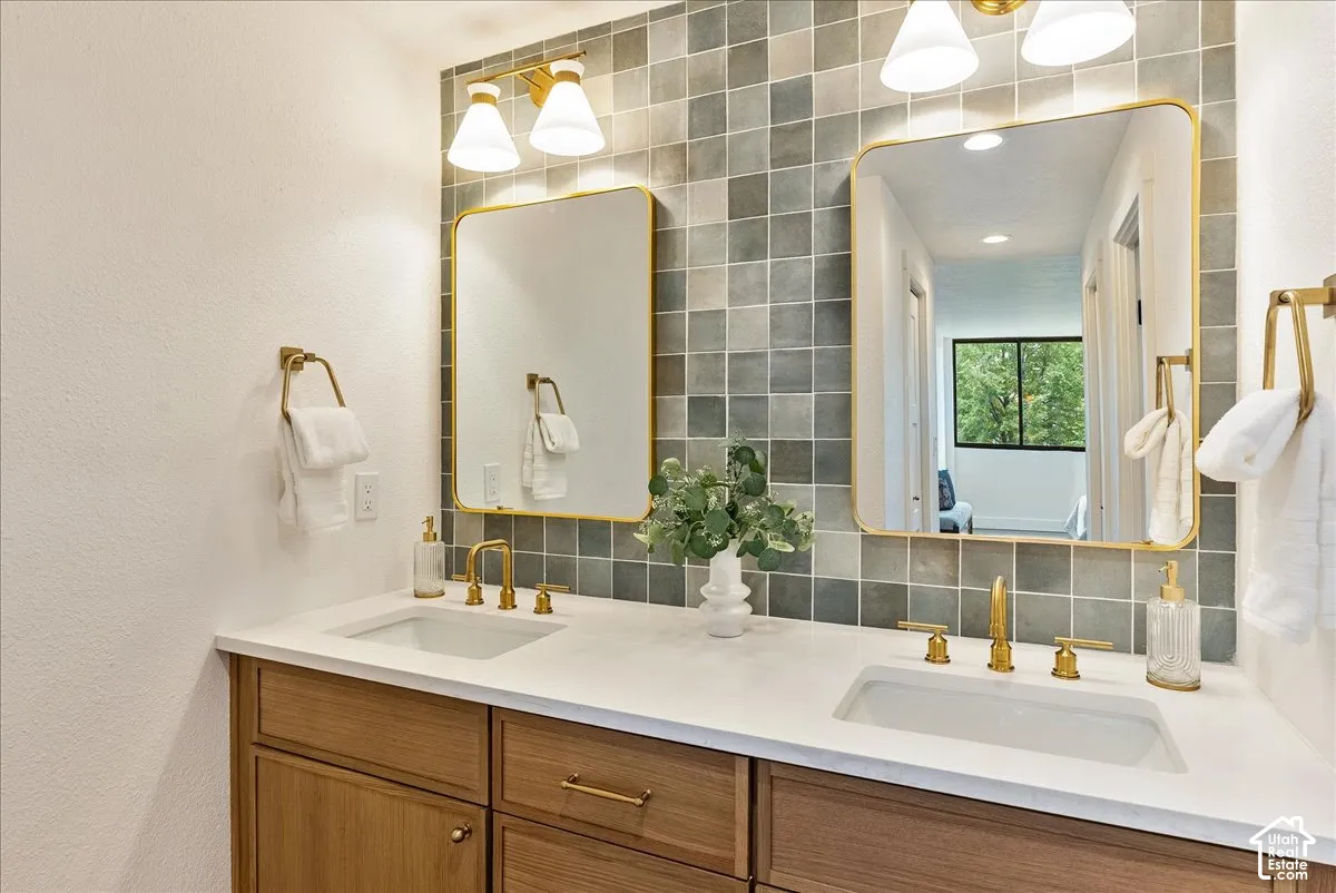 Dual vanity with wood-finish cabinetry, white countertop, and gold-finish fixtures