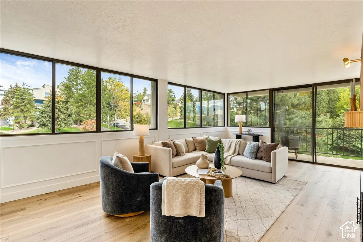 Wood-finish flooring, floor-to-ceiling windows, white paneled wall accents, and an exterior balcony with black railings