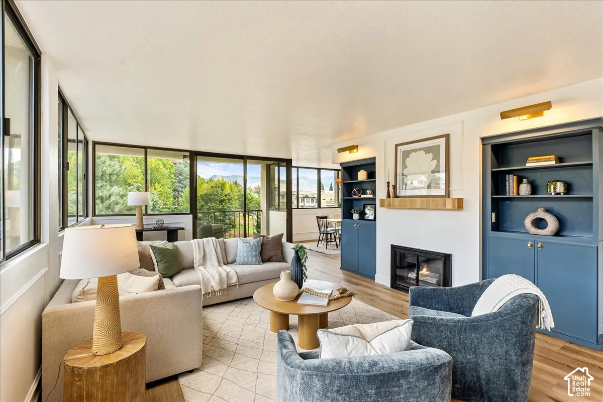 Expansive window wall, wood-finish flooring, built-in shelving, integrated fireplace, and recessed wall sconces