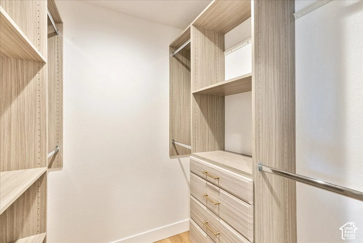 Walk-in closet with custom wood-finish shelving, integrated drawers with gold-tone hardware, and chrome hanging rods