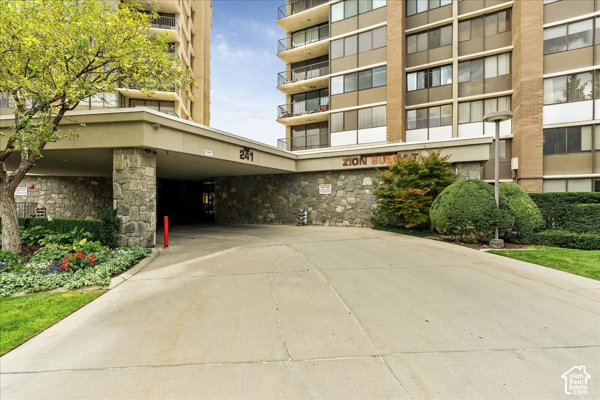 Paved driveway leading to a stone-clad porte-cochere with overhead lighting