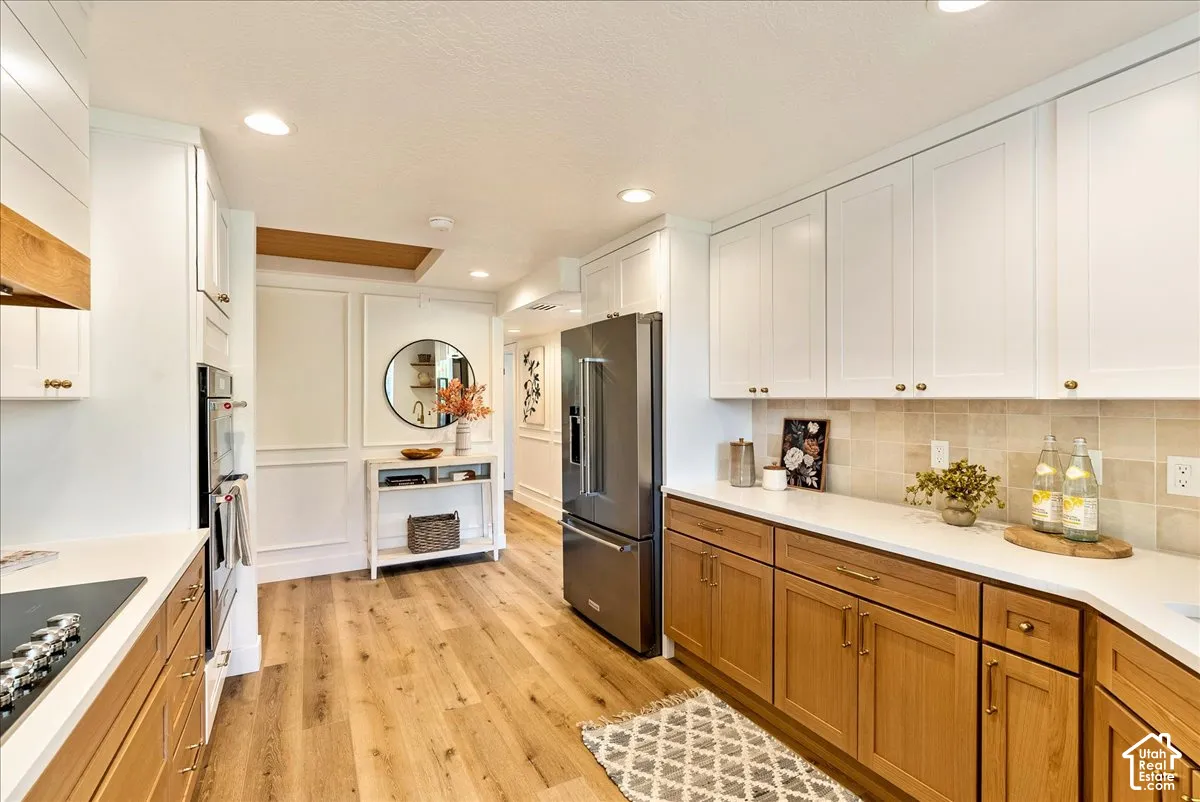 Wood-finish flooring, two-tone cabinetry with brass hardware, light-toned backsplash, integrated oven, and a built-in refrigerator