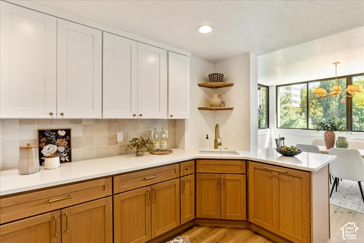 Two-tone cabinetry with white upper and wood-finish lower cabinets, stone countertops, tiled backsplash, and corner shelving with a gold-finish faucet