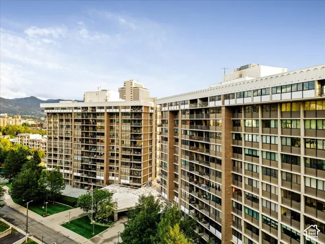 High-rise building with multiple private balconies, a ground-level entrance with a covered drop-off area, and surrounding green spaces