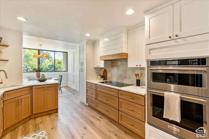Modern kitchen featuring wood-finish flooring, white perimeter cabinetry, wood-tone island cabinetry, stainless steel built-in double ovens, and a tile backsplash