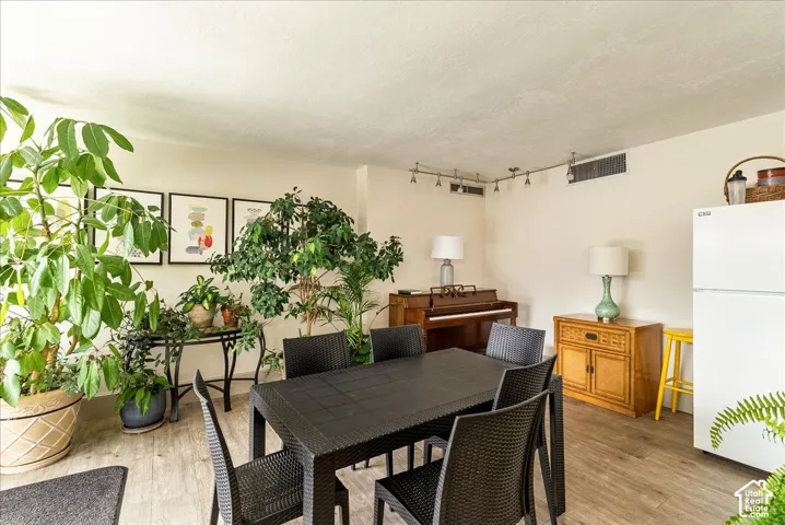 Spacious room with wood-finish flooring, track lighting, and a white refrigerator