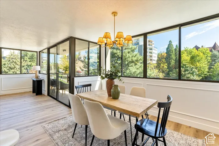 Wood-finish flooring with a decorative area rug, extensive window line, black framed sliding glass doors, white wainscoting, and a central chandelier