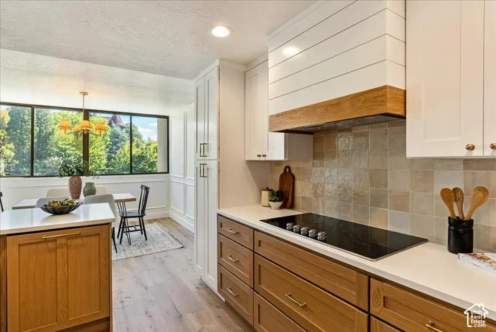 Custom range hood with shiplap detail, integrated cooktop, white countertops, and wood-finish cabinetry