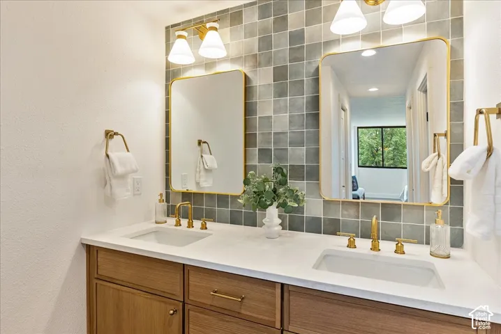 Dual vanity with wood-finish cabinetry, white countertop, and gold-finish fixtures