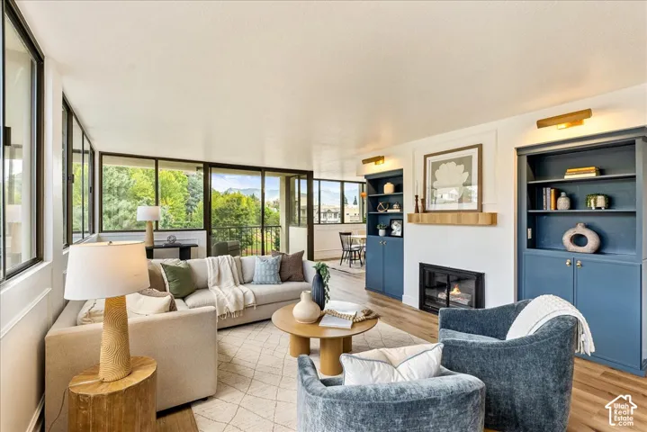 Expansive window wall, wood-finish flooring, built-in shelving, integrated fireplace, and recessed wall sconces