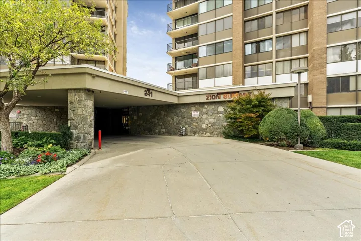 Paved driveway leading to a stone-clad porte-cochere with overhead lighting
