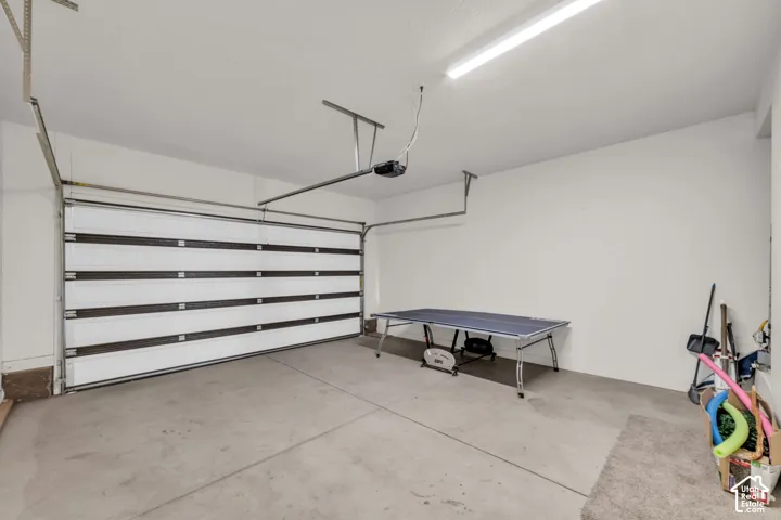 Concrete flooring, white walls, overhead lighting, and an automatic garage door opener