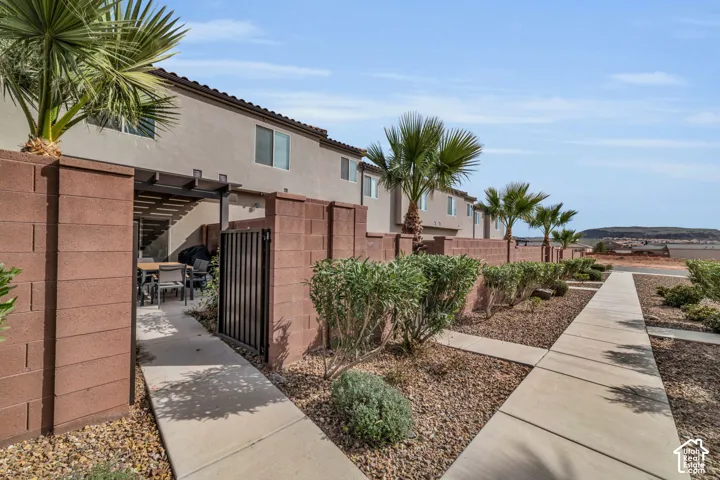 Private outdoor patio with a pergola and block wall fencing, accessed via a concrete pathway and gated entry