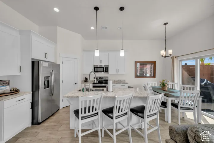 Open-concept kitchen featuring white cabinetry, stainless steel appliances, and an island with bar seating