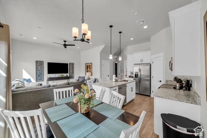 Open-concept living space featuring a kitchen with white cabinetry and light-toned countertops, stainless steel appliances, a central island with an undermount sink, and wood-finish flooring