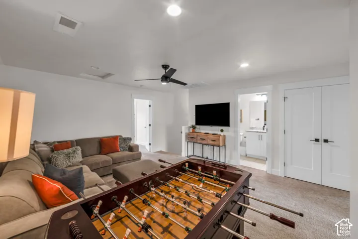 Recessed lighting, ceiling fan, carpet flooring, a built-in television, and an adjacent bathroom with a vanity