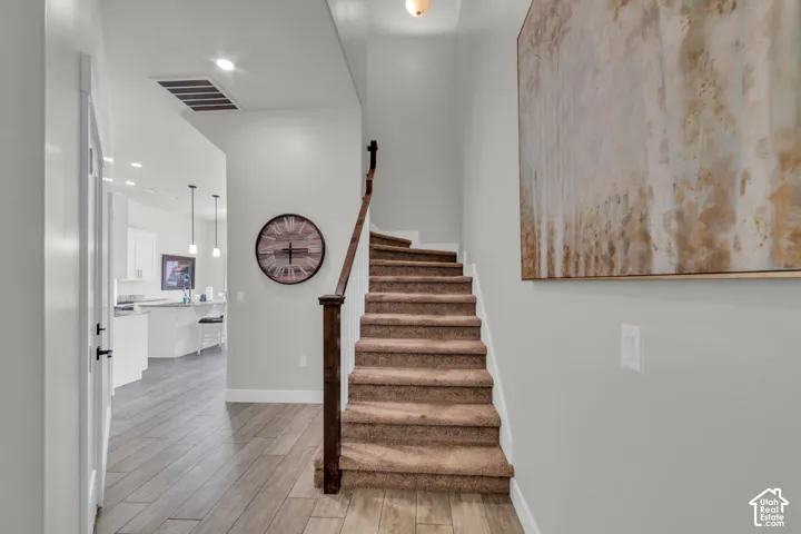 Wood-finish flooring, carpeted staircase with dark wood newel post and handrail, recessed lighting, and white walls