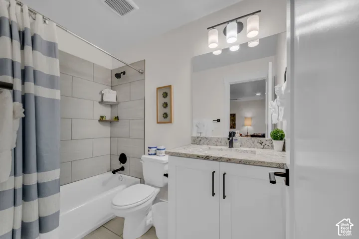Bathroom featuring a bathtub with tile surround, built-in corner shelves, a single vanity with granite countertop, and white cabinetry with dark hardware